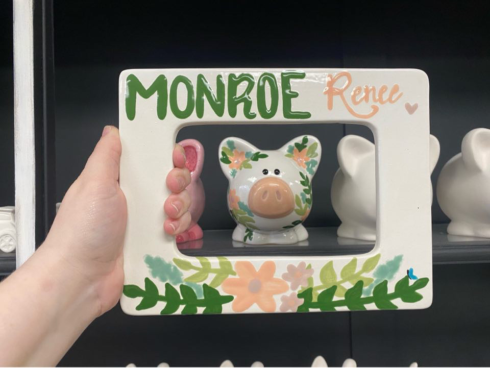 Decorative photo frame with floral design holding a piggy bank, against a dark background.